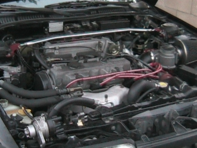 Four-cylinder engine bay with strut tower brace and red plug wires