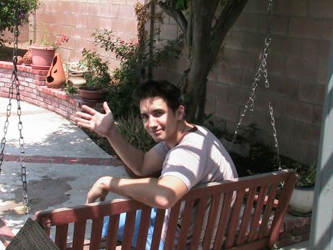 1993 Ford Taurus - A man sits on a porch swing in a backyard setting, waving to the camera.