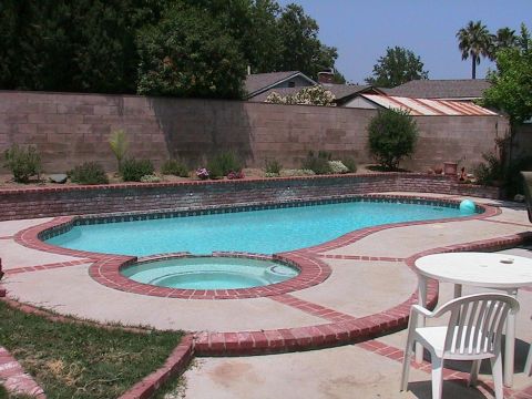 1993 Ford Taurus - A backyard scene a kidney-shaped swimming pool with an attached spa, surrounded by a brick and concrete patio.