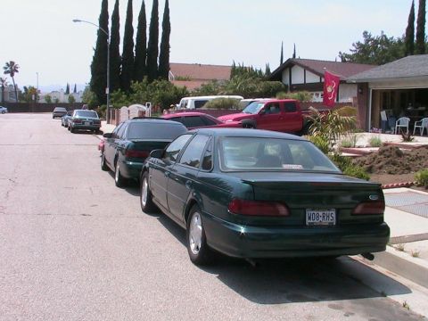 1993 Ford Taurus - Multiple vehicles are parked on a residential street, with a dark green sedan in the foreground.