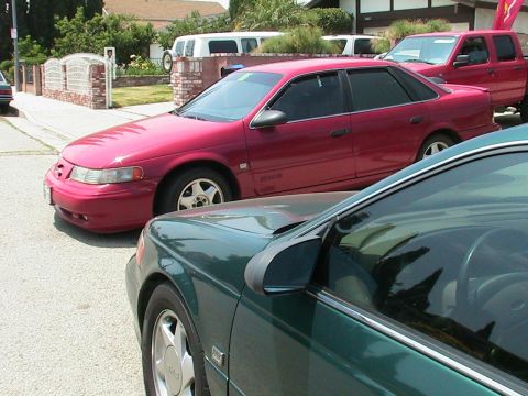 1993 Ford Taurus - A red sedan with tinted windows is parked on a residential street next to other vehicles.