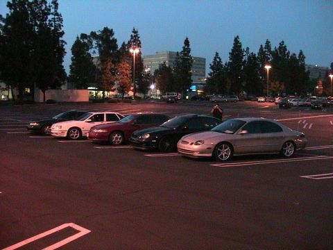 1993 Ford Taurus - A group of cars are parked in a lot as the sky darkens, with a silver sedan prominently displayed.