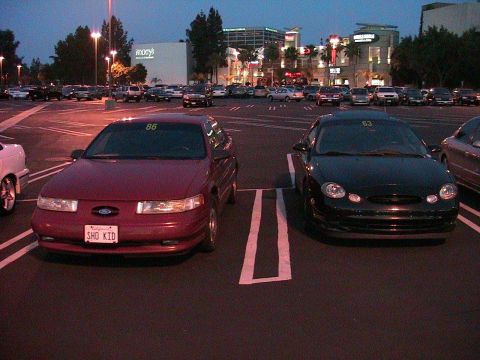 1993 Ford Taurus - Two Ford Taurus sedans are parked in a shopping center lot as evening approaches.