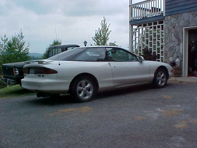 White 1994 Ford Probe coupe, rear quarter view, parked on asphalt next to a black pickup truck