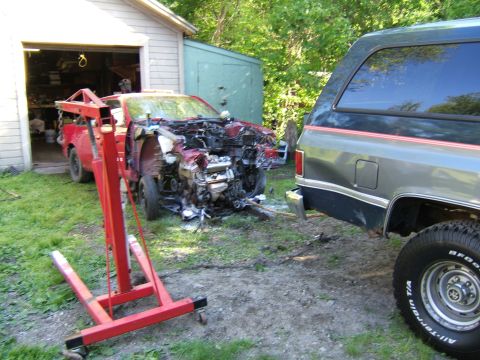 1998 Ford Taurus - A red car with severe front-end damage and its engine exposed sits in a yard next to a dark SUV.