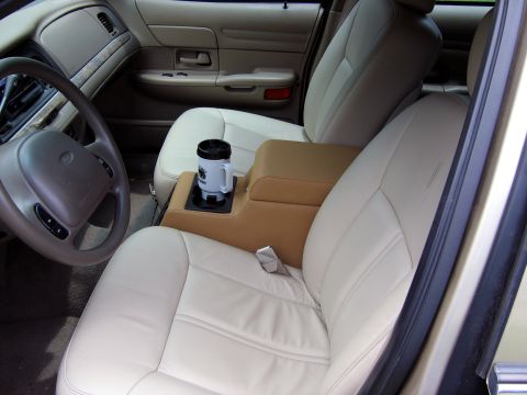 2000 Ford Crown Victoria - Front interior of a Ford Crown Victoria seen through the open driver's door, with light tan leather bucket seats and a darker tan center co…