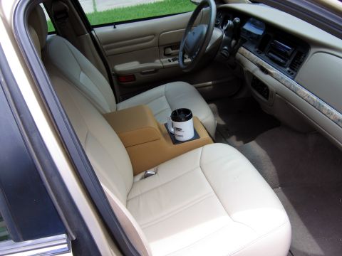 2000 Ford Crown Victoria - The interior of a car features light-colored leather seats and a tan center console with a cup holder.
