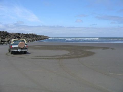 1979 Ford Bronco - A Ford Bronco leaves tire tracks in the sand on a beach with the ocean in the background.