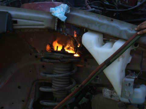 1998 Ford Taurus - A mechanic uses a torch to work on a vehicle's shock absorber and spring assembly in the engine bay.