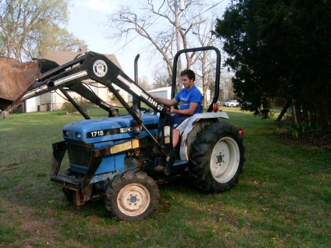 1987 Chevrolet C/K Pickup - A young man operates a New Holland 1715 tractor equipped with a front loader in a grassy yard.