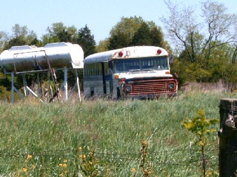 1987 Chevrolet C/K Pickup - A vintage school bus sits in a grassy field next to a large water tank.
