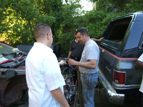 1998 Ford Taurus - Men are working on a car engine next to a dark SUV.