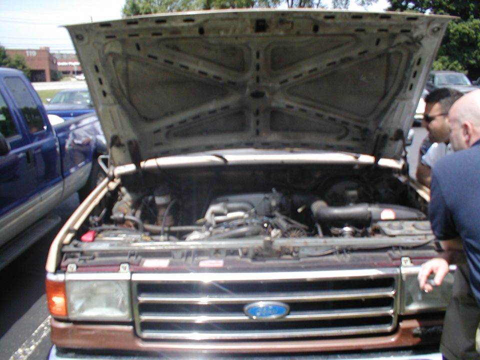 Ford truck engine bay with hood open. Blue truck parked to the left