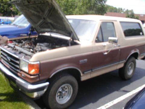 1979 Ford Bronco - This two-tone Ford Bronco has its hood open, revealing the engine bay. A blue vehicle is parked behind it.