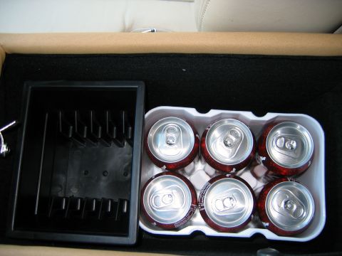2000 Ford Crown Victoria - Looking down into a car's carpeted console storage bin lined with black felt, holding a six-pack of dark red soda cans in a white plastic r…