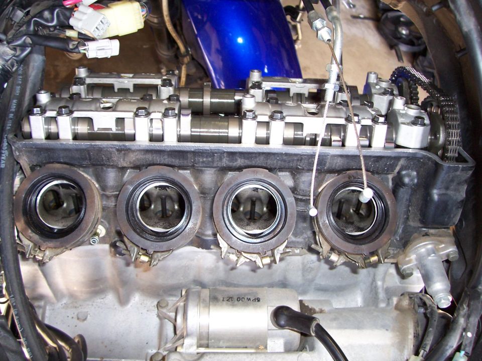 Inline-four motorcycle engine with cam cover off and four open intake ports