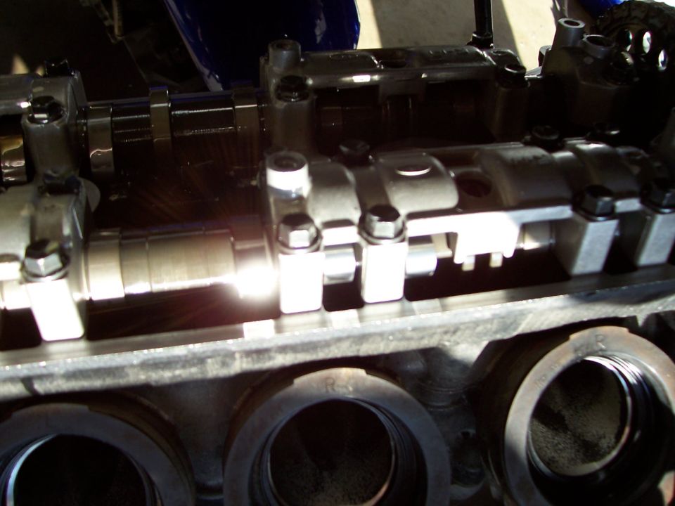 Motorcycle engine top end with valve cover off, exposing dual camshafts and cylinder bores