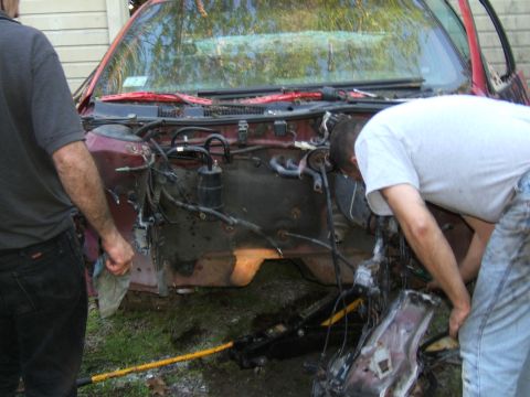 1998 Ford Taurus - Two individuals are working on the engine bay of a 1998 Ford Taurus.