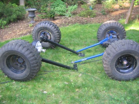 1978 Ford Bronco - Two solid axle assemblies laid out on a lawn, each fitted with mud-terrain tires on black steel wheels and long radius arms, the near axle…