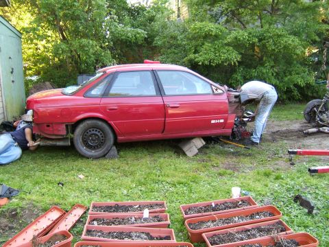 1998 Ford Taurus - Two people work on a red 1998 Ford Taurus that has had its rear end removed.