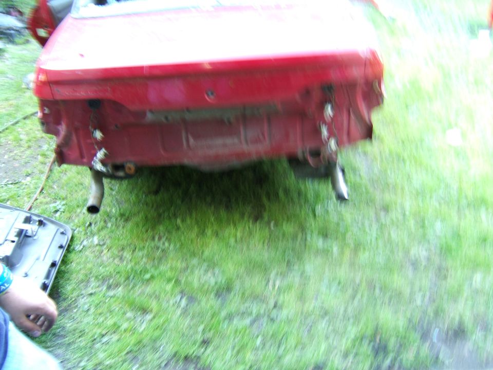 Rear of a red car, bumper removed, showing exhaust pipes and frame