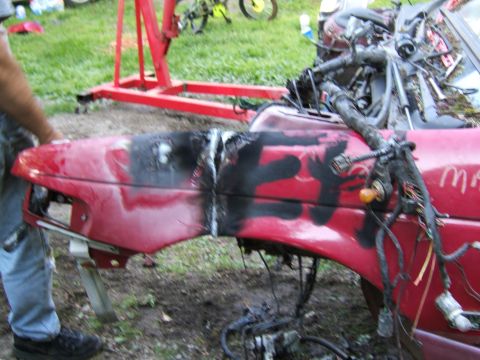 1998 Ford Taurus - A red car fender, heavily marked with black spray paint and showing exposed wiring, is being worked on outdoors.