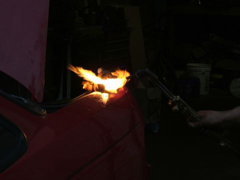 1998 Ford Taurus - A torch is being used to cut or weld on the hood of a red car in a dimly lit garage.