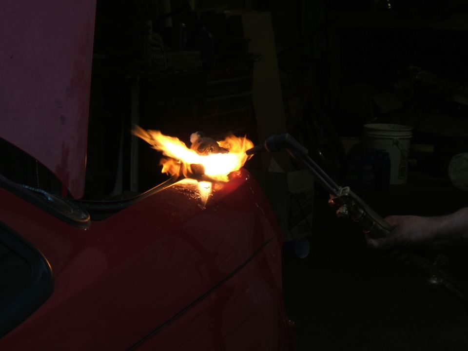 Someone is using a torch to cut or weld on the red hood of a car