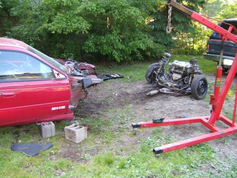 1998 Ford Taurus - A red car has been disassembled, with its engine and front suspension removed and placed on the ground.