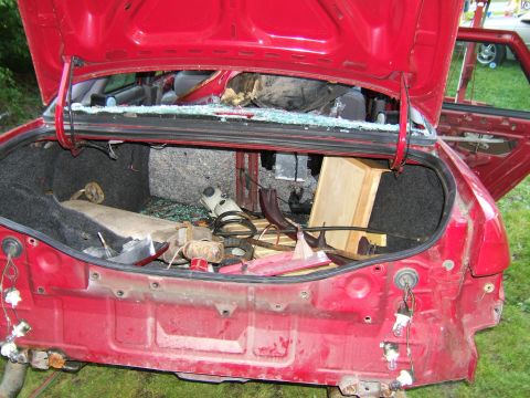 1998 Ford Taurus - The rear of a red 1998 Ford Taurus is shown with the trunk open, revealing damage and debris.