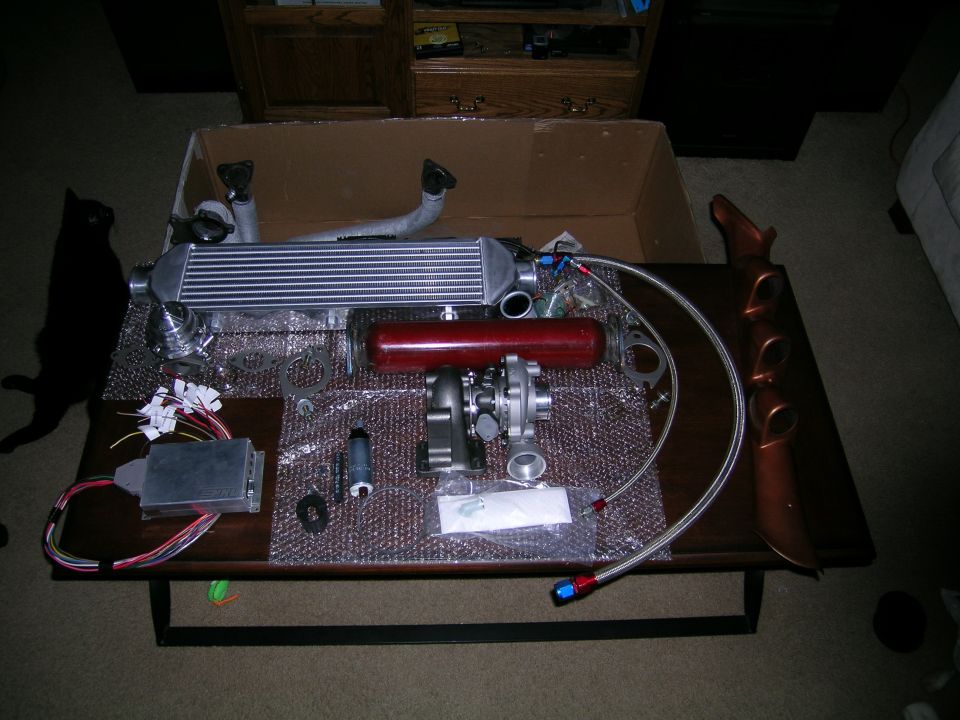 Turbo kit laid out on a table, includes intercooler, turbo, red reservoir, and wiring