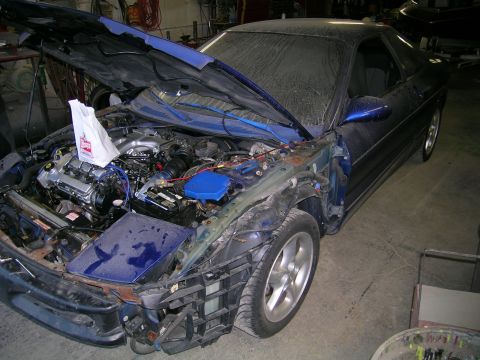 1994 Ford Probe - A blue coupe with its hood open and significant damage to the front end sits in a workshop.