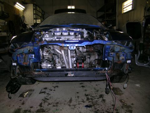 1994 Ford Probe - The front end of a blue car is disassembled in a workshop, revealing the engine and internal components.