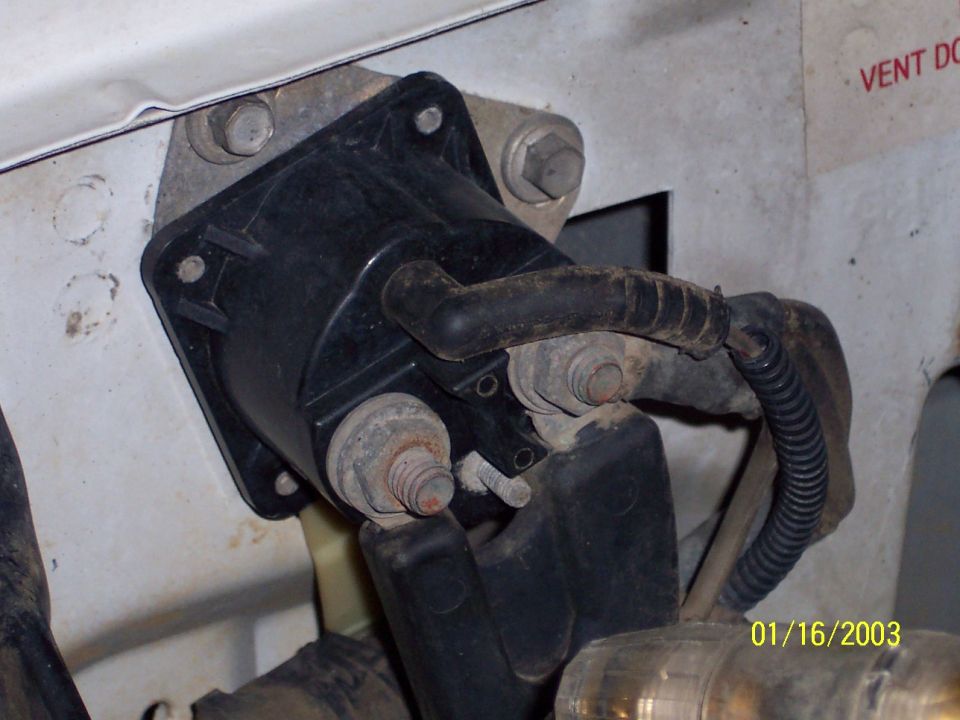 Automotive starter solenoid mounted on white vehicle bodywork, with visible rust on bolts