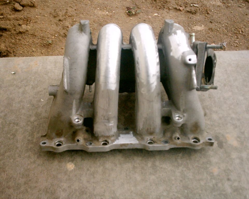 Aluminum intake manifold with four runners, resting on a concrete surface