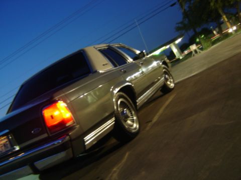 1988 Ford Crown Victoria LTD - The rear of a 1988 Ford Crown Victoria LTD is visible at dusk, with its taillights illuminated.