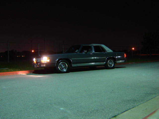 Dark sedan with a white roof, parked at night. Headlights are on