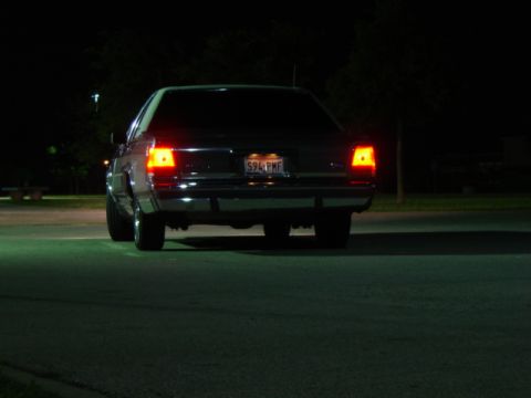 1988 Ford Crown Victoria LTD - Rear view of a dark sedan at night, showing its illuminated taillights and license plate.