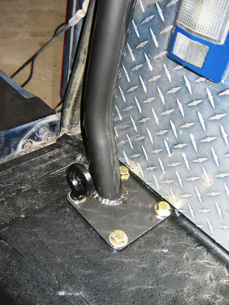 Black roll bar foot welded to a plate and bolted to floor beside diamond-plate panel.