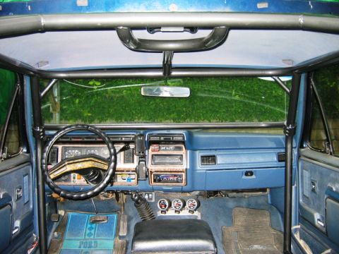 1985 Ford Bronco - The interior of this Ford truck features a prominent roll cage and aftermarket audio equipment.