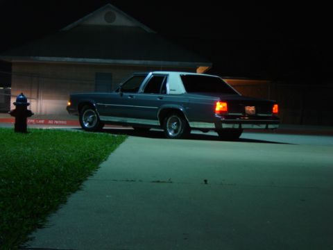 1988 Ford Crown Victoria LTD - A dark blue sedan with a white vinyl roof is parked at night, showing its rear lights and chrome bumper.