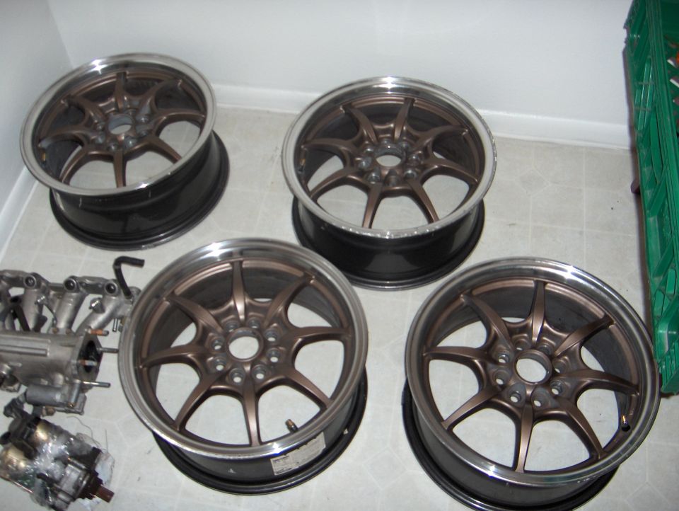 Four bronze 7-spoke alloy wheels with polished lips on a tile floor beside an intake manifold.