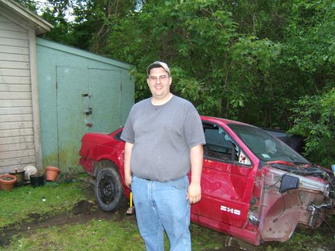 1998 Ford Taurus - A man poses with a heavily damaged red 1998 Ford Taurus in a yard.