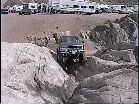1997 Chevrolet C/K Pickup - A pickup truck is shown off-roading over large rocks, with a campsite visible in the distance.