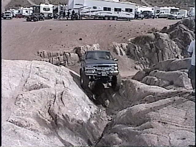 Pickup truck navigating a rocky trail, with RVs and other vehicles in the background