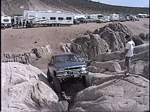 1997 Chevrolet C/K Pickup - A blue pickup truck is off-roading through a rocky landscape with other vehicles and RVs in the background.