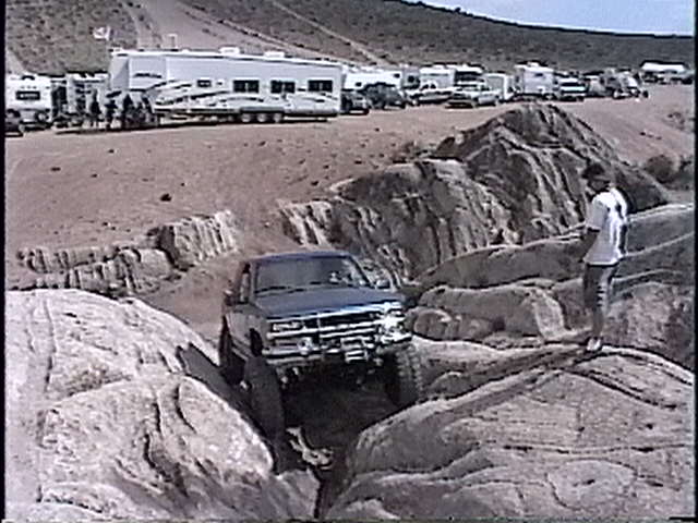 Blue pickup truck navigating rocky terrain, front grille visible
