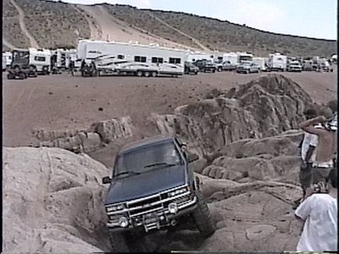 1997 Chevrolet C/K Pickup - A pickup truck maneuvers through a rocky obstacle course with RVs and trailers visible in the distance.