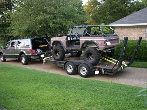 1995 Ford Bronco - A Ford Excursion tows a brown Ford Bronco on a trailer, both vehicles are on a paved driveway.