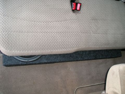 1999 Ford F-150 - A subwoofer box is installed beneath the seat of a vehicle, with a seatbelt buckle visible above.